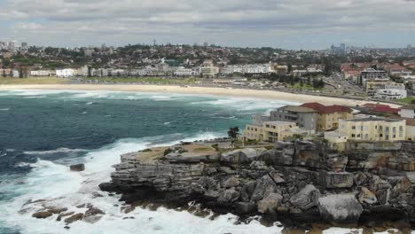 Costa-Irregular-Con-Horizonte-De-Sidney-Y-Playa-De-Bondi-Bay-Y-Olas-Tormentosas-Rompiendo-En-Un-Acantilado-En-Australia