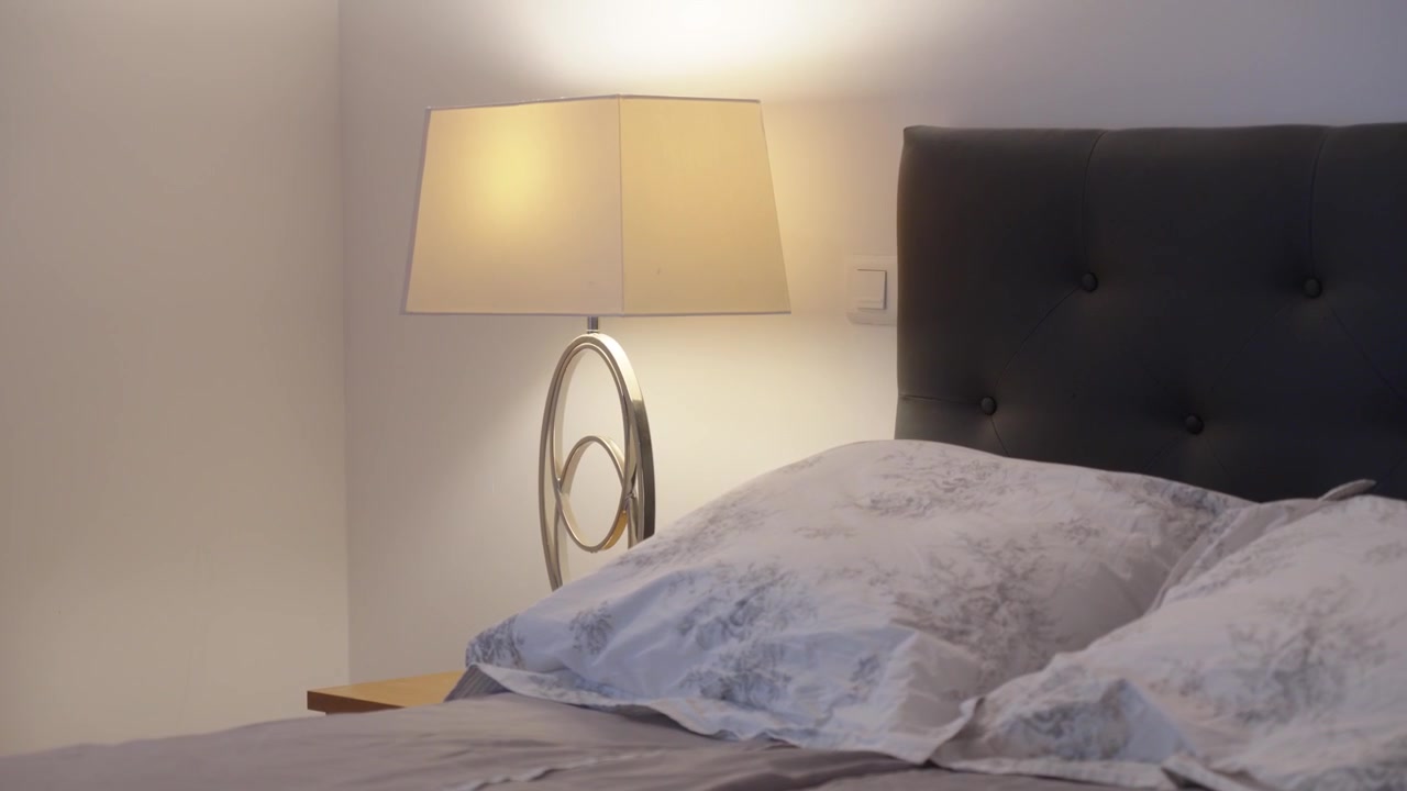 in a modern adult bedroom, the sleeping area with a close-up of the bedside table and a stylish lamp giving off a soft glow, along with pillows and crumpled bed sheets