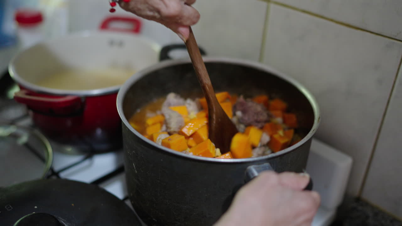 Cook slowly stirs steaming argentina's locro in heavy pot revealing chunks of butternut pumpkin, chorizo sausage, onions, corn kernels simmering in rich stock, aromas rising in a rustic home kitchen