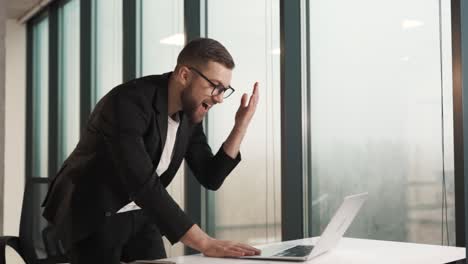 hombre apasionado que trabaja en la computadora portátil mientras está de pie en la oficina