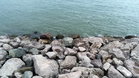 aerial view above splashing ocean tide breaking on rocky coastal shoreline slow left dolly