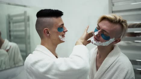 pareja masculina divirtiéndose, aplicando espuma de afeitar haciendo rutina matutina juntos en el baño