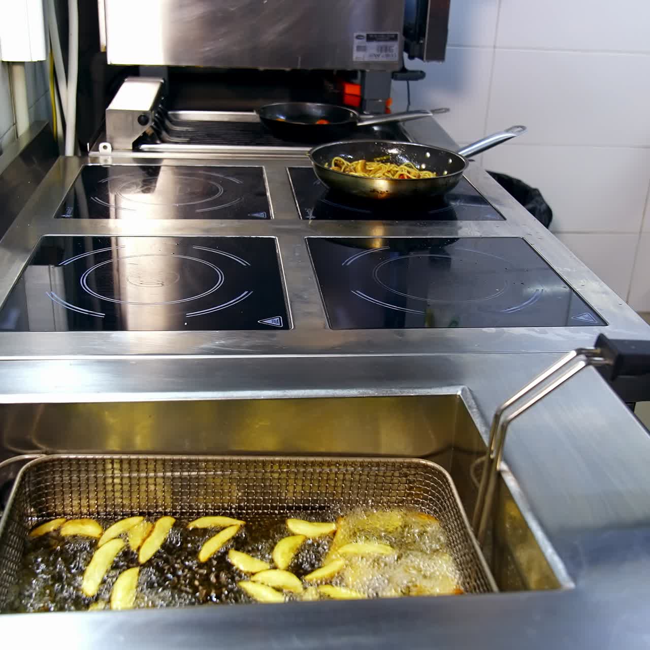 Fritadeira na cozinha do restaurante. O chef cozinha alimentos na frigideira. Batatas crocantes fritando em óleo quente e fervente. Refeições deliciosas.
