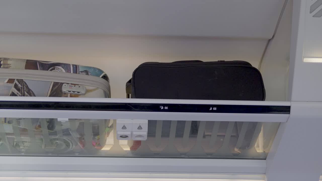 Inside a train, a black bag is placed next to a suitcase in an overhead compartment