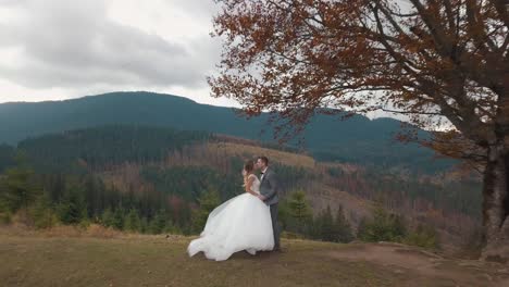 Lovely-young-newlyweds-bride-and-groom-embracing,-making-a-kiss-on-mountain-slope,-wedding-couple