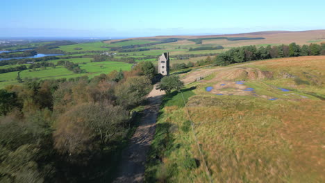 flying fast over track towards lone stone tower building on hillside with reveal of countryside beyond