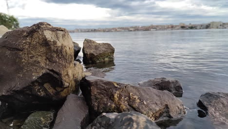 Big-Rocks-Through-Calm-Water-Under-Cloudy-Sky-In-Southbank-River-Of-Portugal