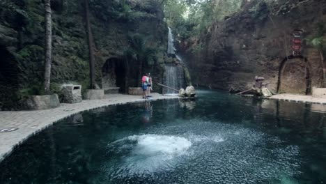 Hombre-Hispano-Saltando-A-Una-Piscina-Natural-Con-Bosque-Al-Fondo