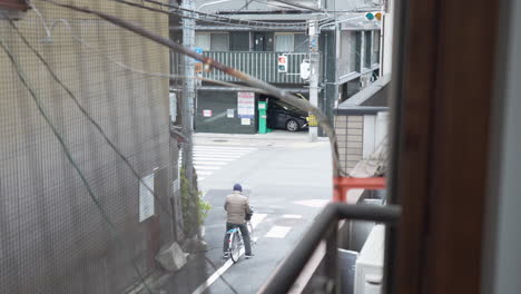 Ein-Fenster-Zu-Den-Typischen-Straßen-Japans:-Ein-Mann-Wartet-Darauf,-Dass-Sich-Der-Verkehr-Bewegt,-Um-Mit-Dem-Fahrrad-Loszufahren