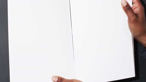 video de la mano de un hombre afroamericano sosteniendo un libro con páginas en blanco, espacio de copia en fondo negro