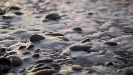 close up beach waves and water streaming through pebbles and rocks slowmo