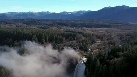 aerial flyover snoqualmie falls waterfall with mist in the valley and beautiful nature landscape with pine trees and mountains in background