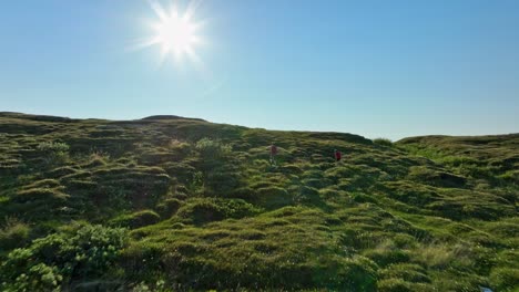 Drone-rising-over-a-man-and-a-boy-hiking-to-the-top-of-a-fell-in-north-Norway,-summer-day