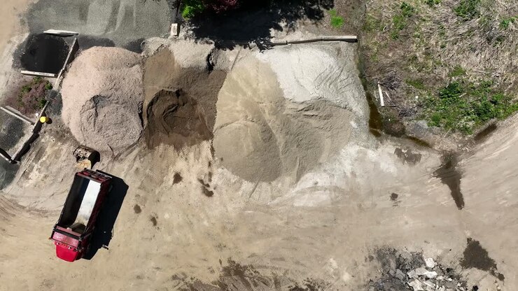 Drone top down pan across empty dump trucks parked by dirt stockpile