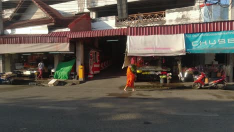 Buddhist-monk-in-orange-robe-walking-next-to-market-in-Chiang-Mai,-Thailand