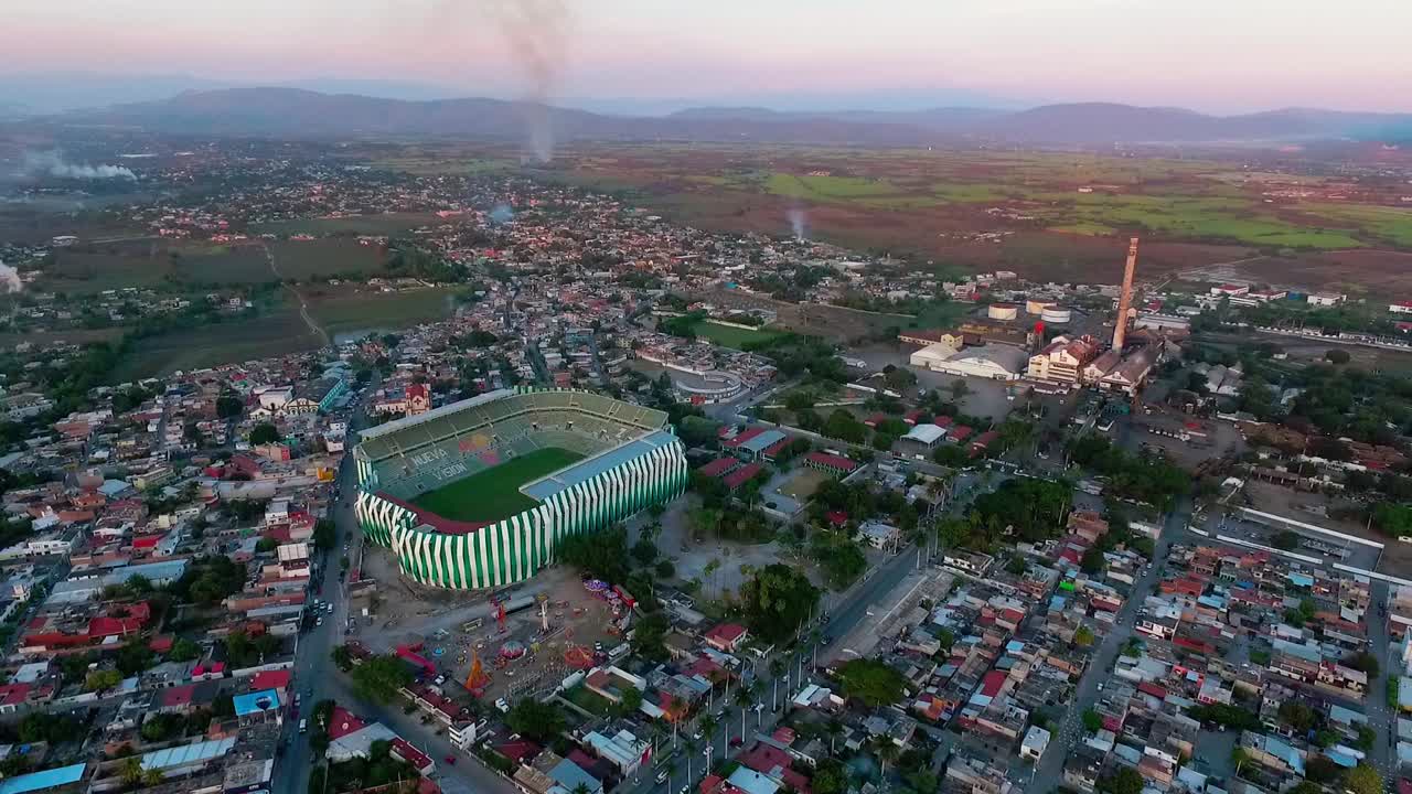 A soccer stadium surrounded by a small town during sunset, vibrant rural landscape, aerial view