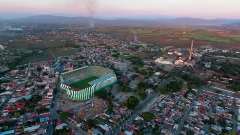 a soccer stadium surrounded by a small town during sunset, vibrant rural landscape, aerial view