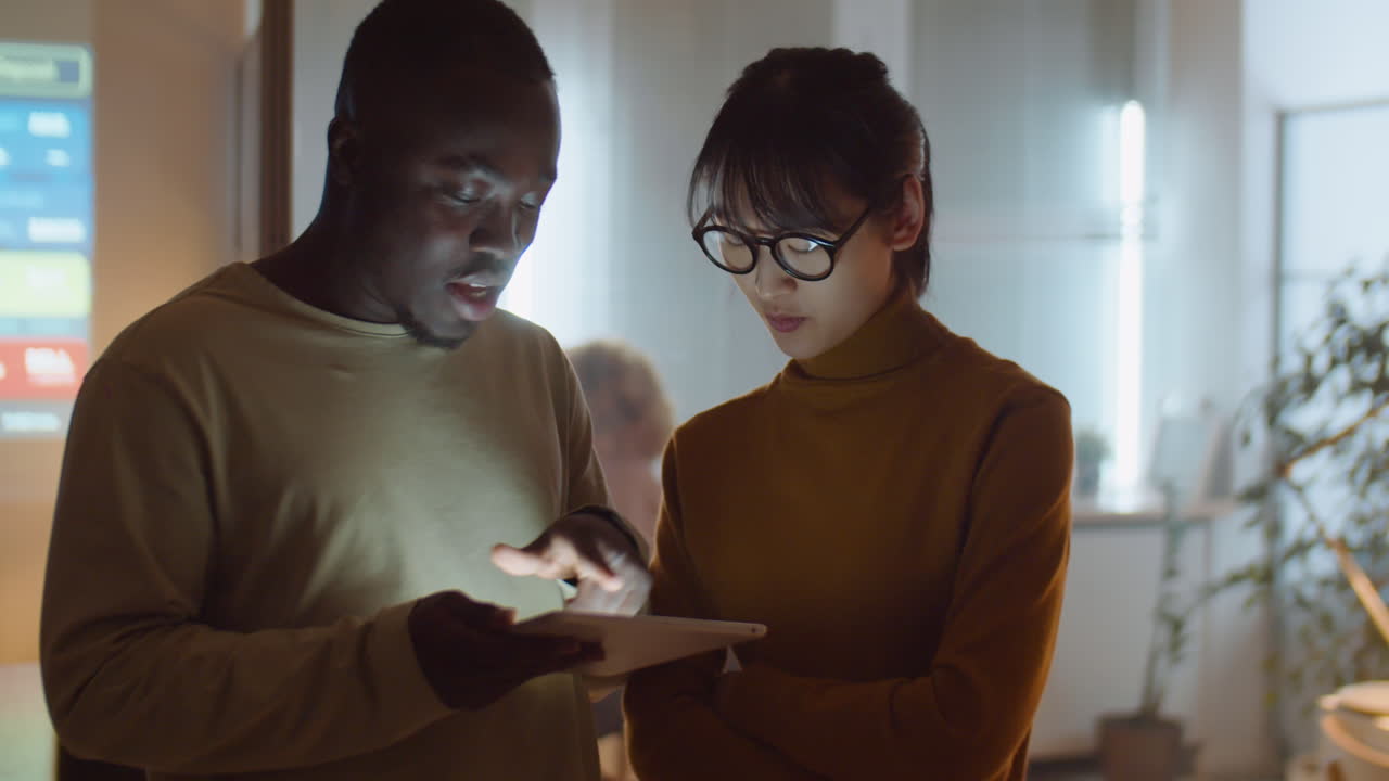 Multiethnic Coworkers Using Tablet and Speaking in Office at Night