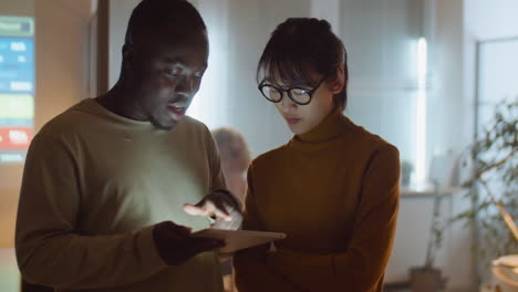compañeros de trabajo multiétnicos que usan tabletas y hablan en la oficina por la noche