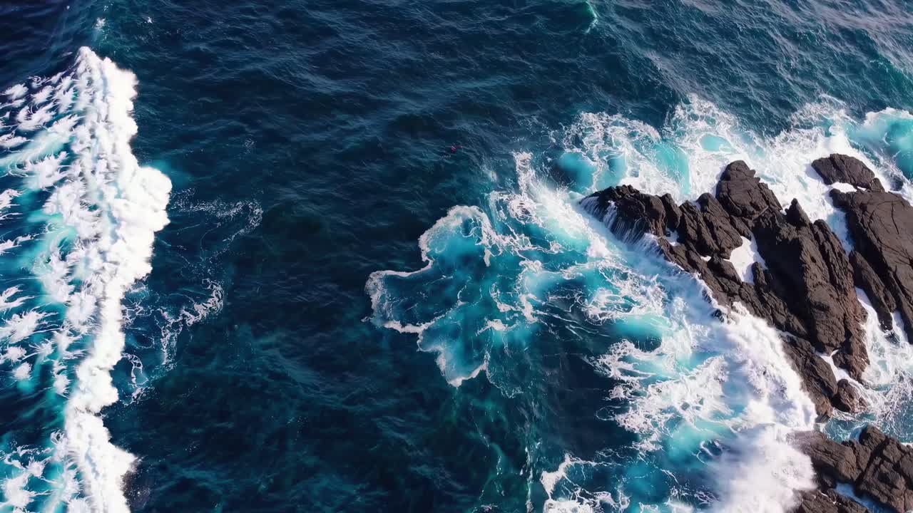 Luchtopnamen van golven die tegen ruige rotsen slaan