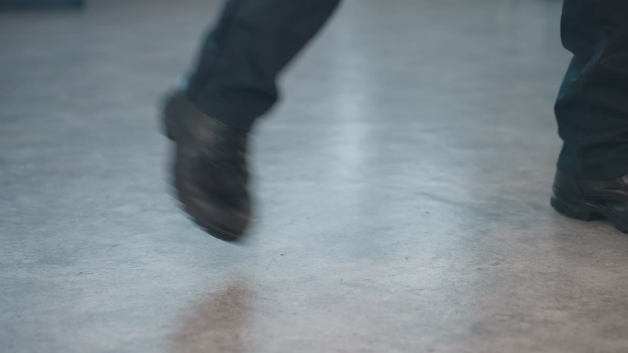 close up of dancer leg in sturdy black boot and slim black trousers tapping precise steps on smooth studio floor showcasing dynamic rhythm and sleek style in modern minimal rehearsal space