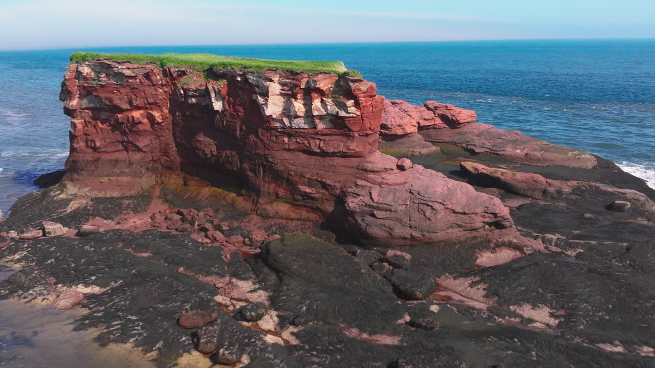 drone flies towards red rock cliffs and over the ocean on a beautiful day