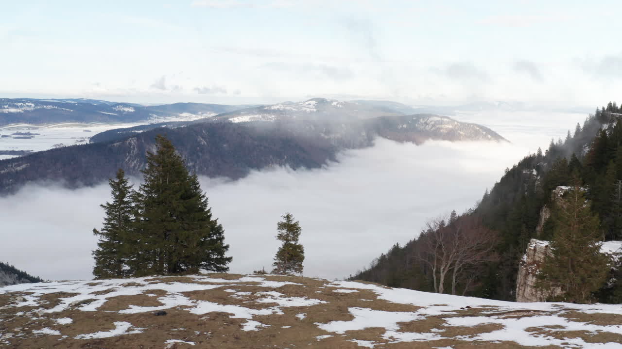 volando sobre la cresta de la montaña, revelando un hermoso valle con nubes bajas