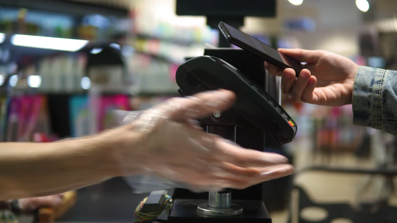 supermercado: mostrador de caja. el cliente paga con el teléfono inteligente por sus alimentos, aplicando el móvil en la terminal inalámbrica. sin rostros. cerca