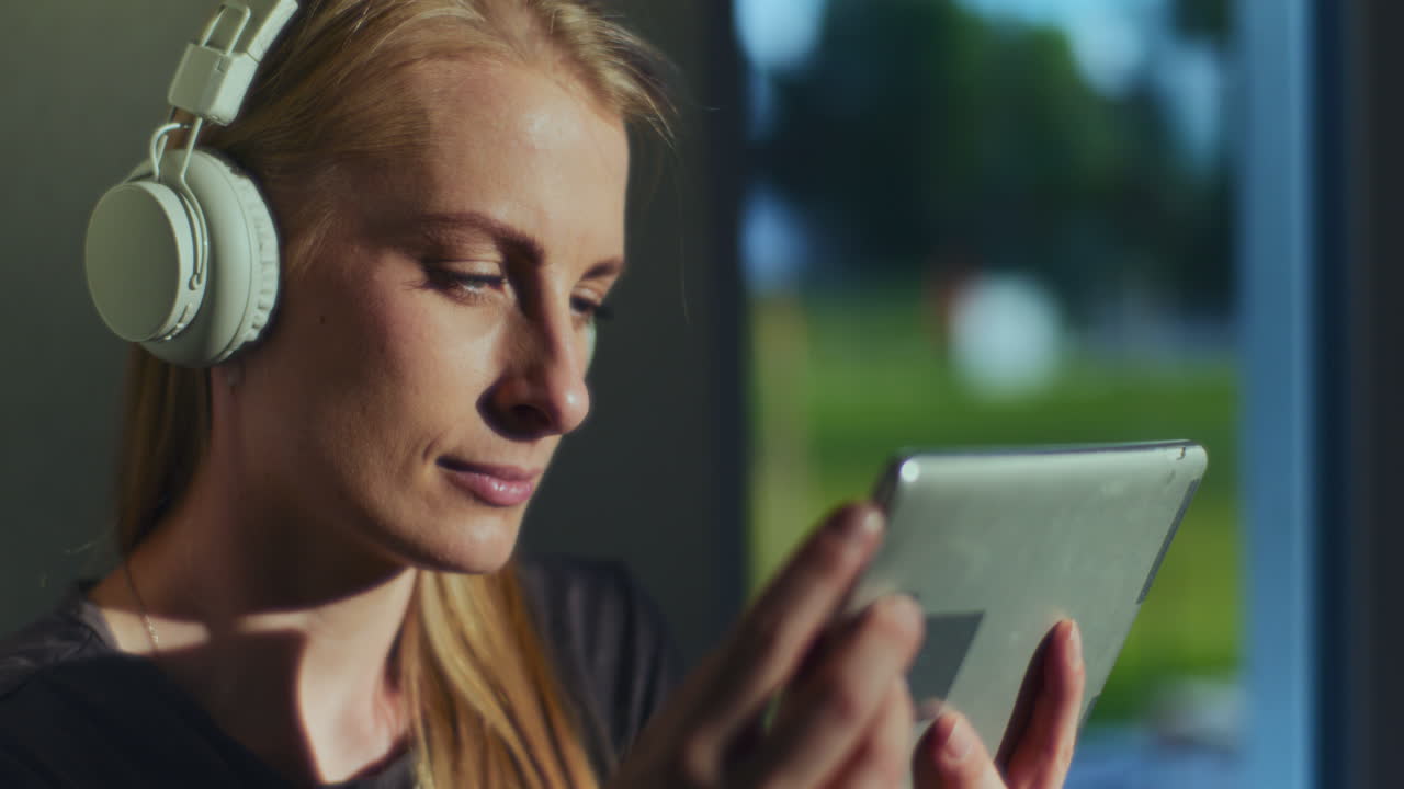 mujer concentrada utiliza tableta digital y auriculares inalámbricos