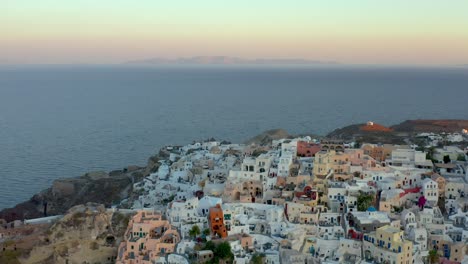 Sobrevuelo-Aéreo-Famoso-Destino,-Encantadora-Ciudad-De-Oia-En-Las-Luces-Del-Amanecer,-Santorini