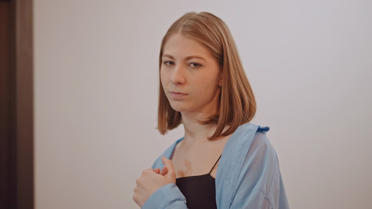 Caucasian woman music student clasping hands. Nervous expression before audition, denim jacket, waiting in hallway, mentor support offframe, soft natural light and quiet anticipation