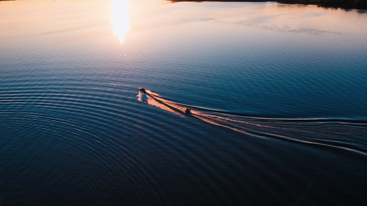 Motor boat on water at sunset. Panoramic view of the evening river with two boats. Motor boat pulling small boat with people. View from above.