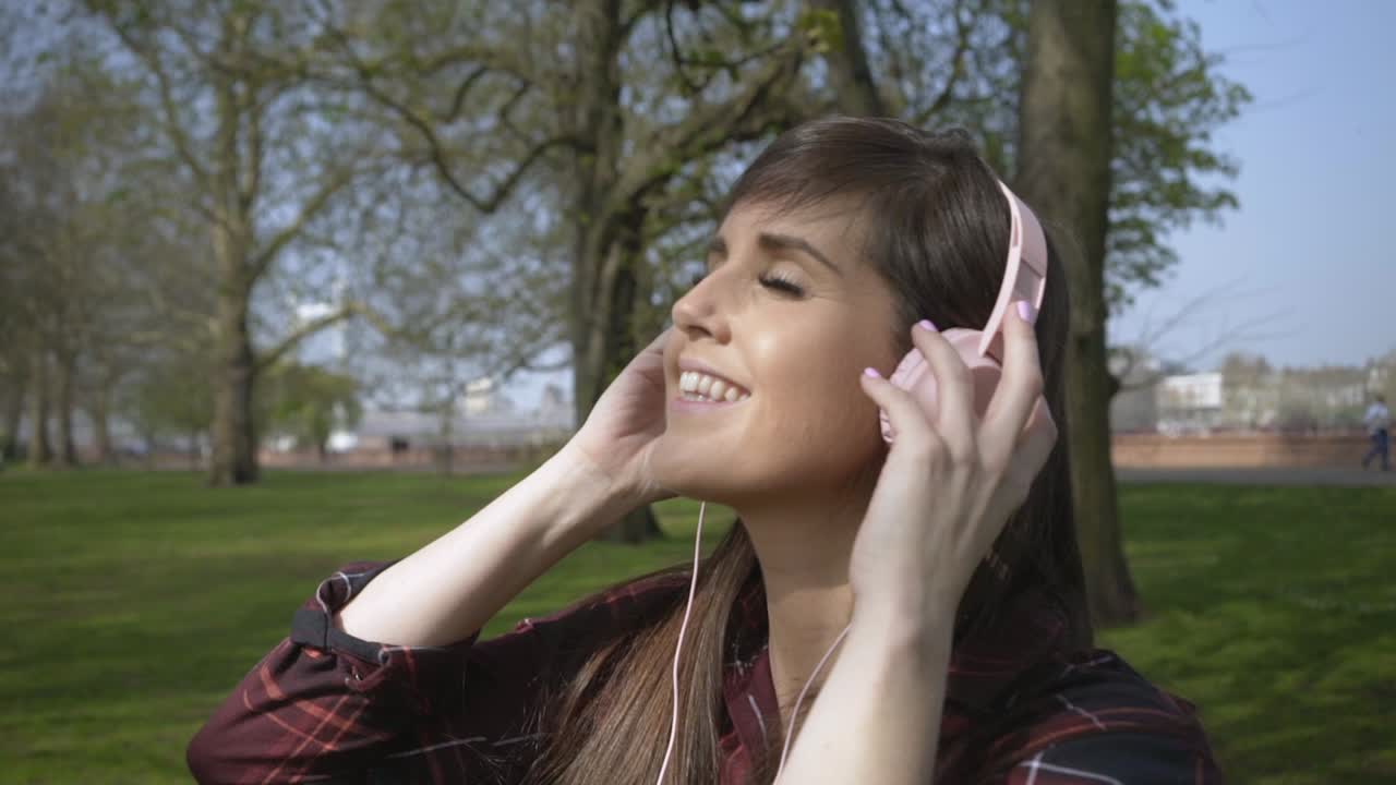 mujer caucásica escuchando música a través de auriculares en cámara lenta en un parque