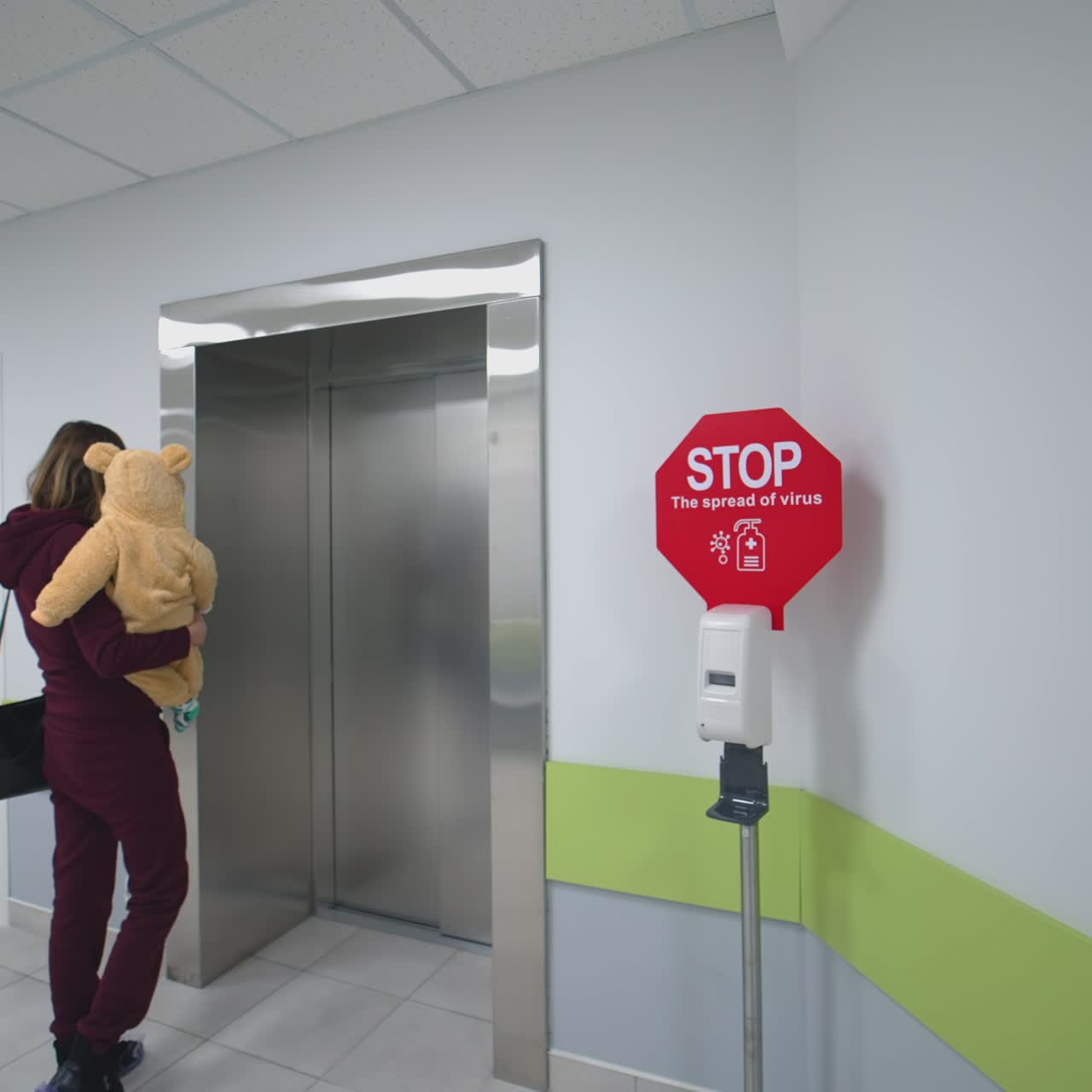 Disinfettante con segnale di stop in clinica. Donna con un bambino si avvicina all'ascensore vicino al segnale di avvertimento sulla diffusione del virus in ospedale. Epidemia di virus.