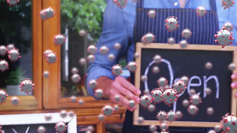 animation of macro covid-19 cells floating over happy caucasian male chef holding open sign