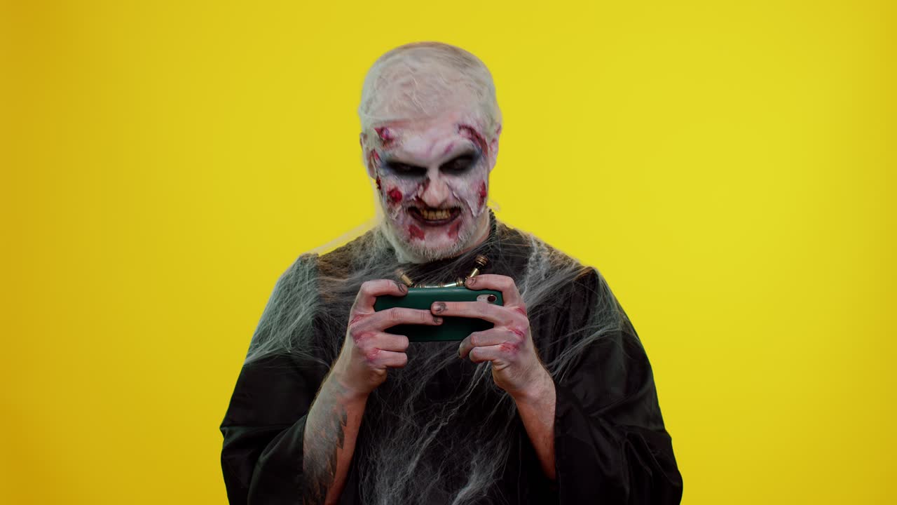Uomo sinistro zombie di Halloween che gioca con entusiasmo a videogiochi di corsa sul cellulare