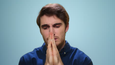 hombre enfocado diciendo oración en el estudio. chico guapo orando en fondo azul