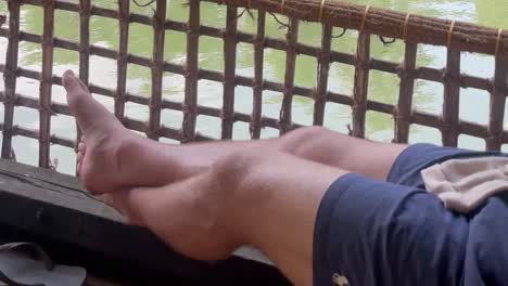 4k video of a man's legs while enjoying a ride on a boat in the backwaters of kerala, india