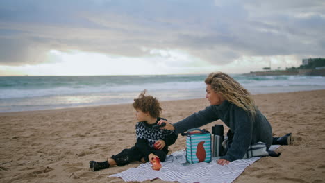 Mom-son-playing-picnic-looking-spyglass-on-cloudy-shore.-Excited-kid-dreaming