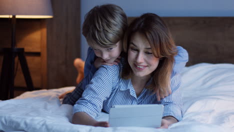 Caucasian-charming-woman-doing-or-watching-something-on-the-tablet-while-his-small-son-looking-out-over-her-shoulder