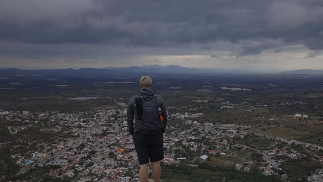 hombre turista mirando la vista de la aldea mexicana, dramáticas nubes grises en el horizonte