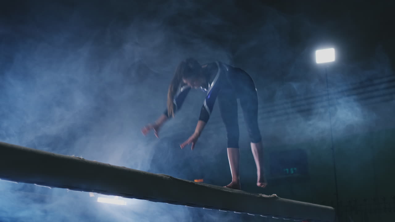 Legs Professional girl gymnasts jump in slow motion in the smoke on the balance beam. Women's Artistic Gymnastics