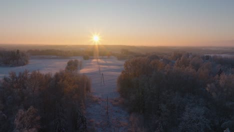 Aerial-establishing-view-of-a-rural-landscape-in-winter,-snow-covered-countryside-fields,-cold-freezing-weather,-sunset-with-golden-hour-light,-wide-drone-shot-moving-forward