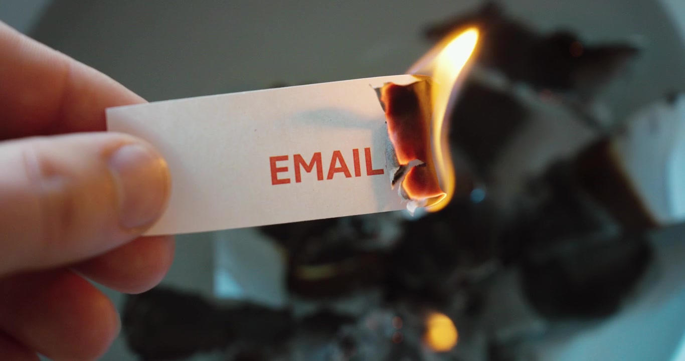 Primo piano di un foglio con la scritta "email" che brucia, a simboleggiare il sovraccarico della casella di posta, lo stress e la riduzione del disordine digitale.