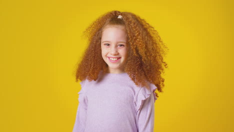 studio portrait of smiling girl with red hair against yellow background