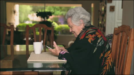 mujer de edad con gadget sentado en la mesa