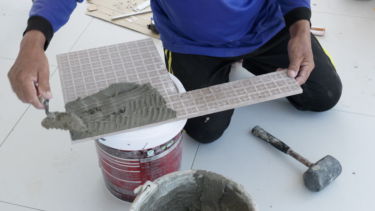 Spreading mixed mortar of cement and fine sand, a construction worker is preparing to lay the ceramic tile on the floor