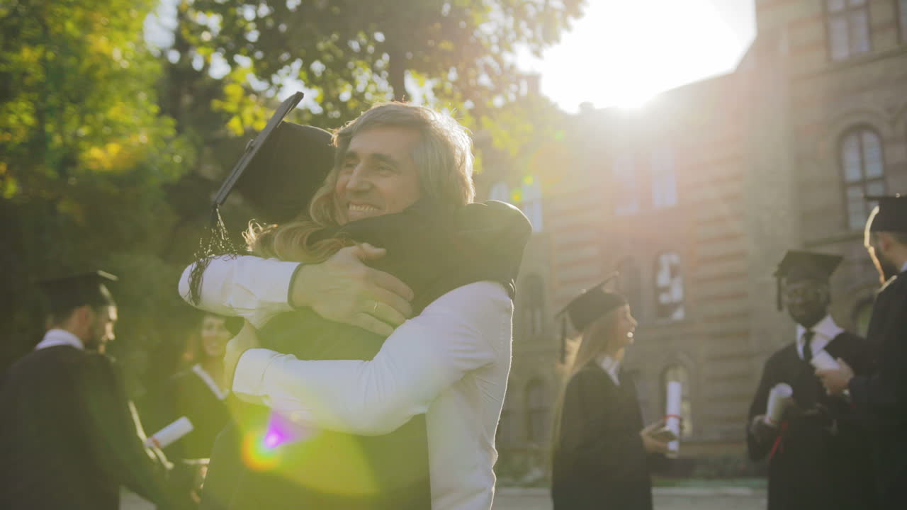vista trasera de la graduada rubia que se felicita con la graduación de su padre canoso en un día soleado