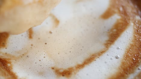 close-up of a person dipping a biscuit into a creamy latte