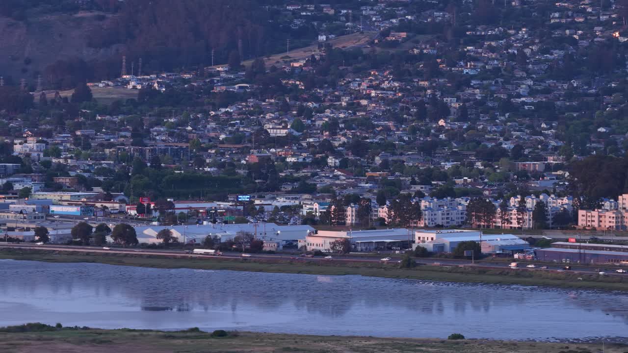 Ampia vista aerea di Albany, California, con le luci della città che iniziano a illuminare il paesaggio urbano e le colline circostanti mentre il crepuscolo cala sulla costa della baia di San Francisco
